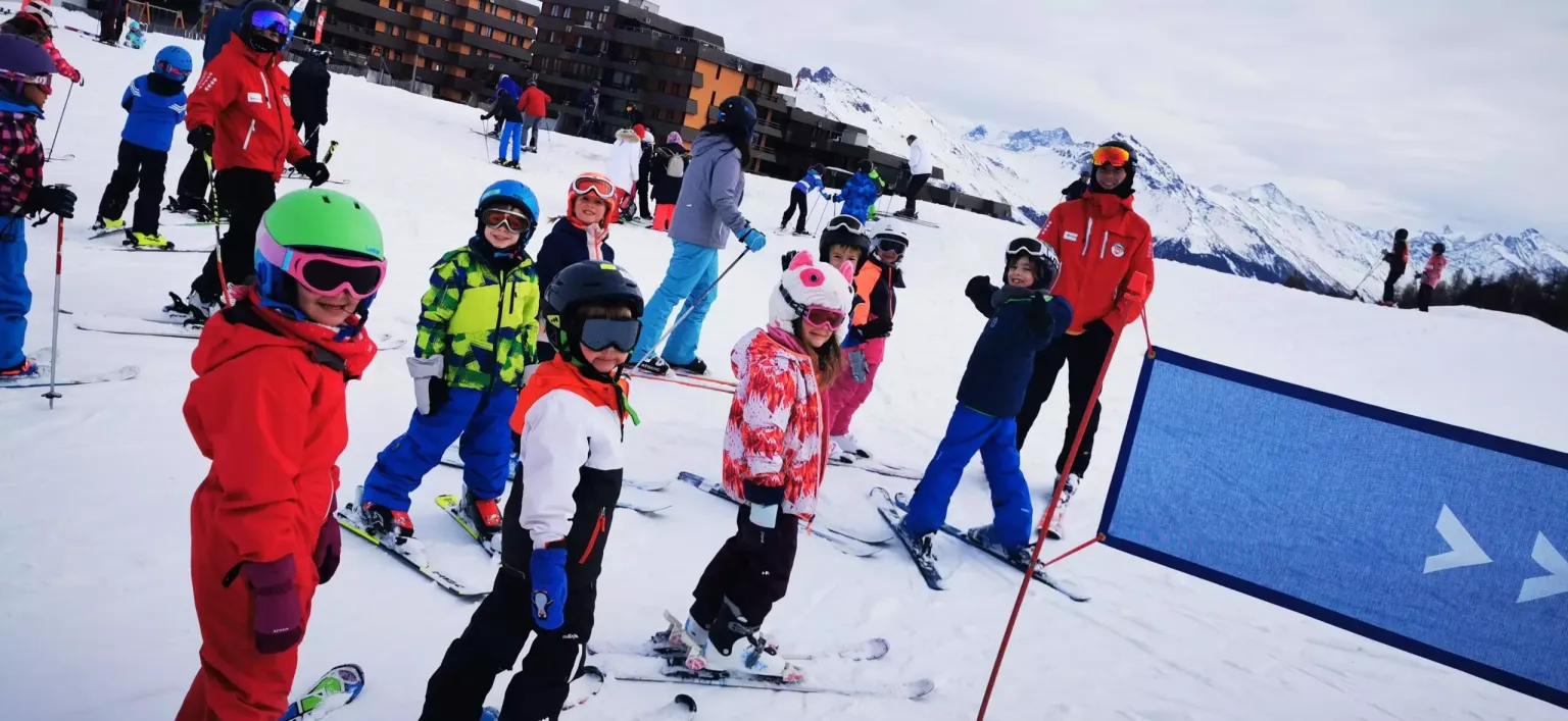 Groupe d’enfants avec moniteur de ski ESS sur les pistes en montagne – Kids Trip Swiss